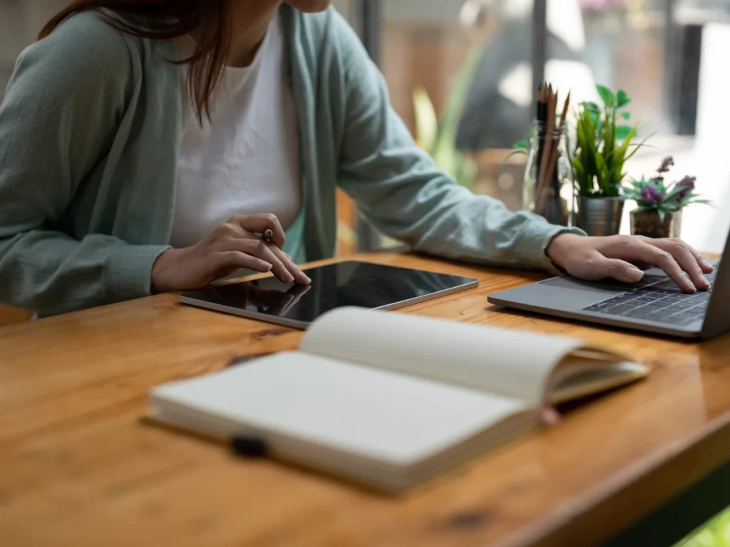 Woman studying online with a tablet, laptop, and open notebook on desk 
